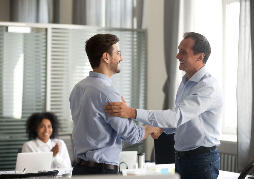 two people shaking hands with someone sitting the background